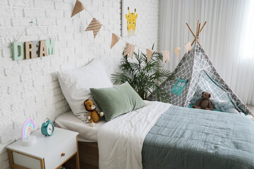 Childhood development and nursery interior, cozy bedroom with teepee tent and soft toys for kids in a modern home with white brick wall decor © Pixel-Shot