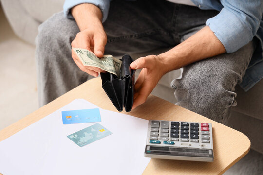Financial struggle and poverty, man counting cash from wallet with credit cards and calculator for budget planning and debt management at home