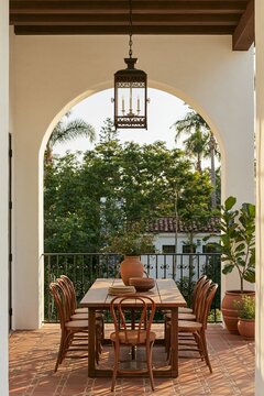 Wrought iron pendant lantern illuminating a wooden dining table on a Spanish Revival villa patio with terracotta tiles and lush greenery