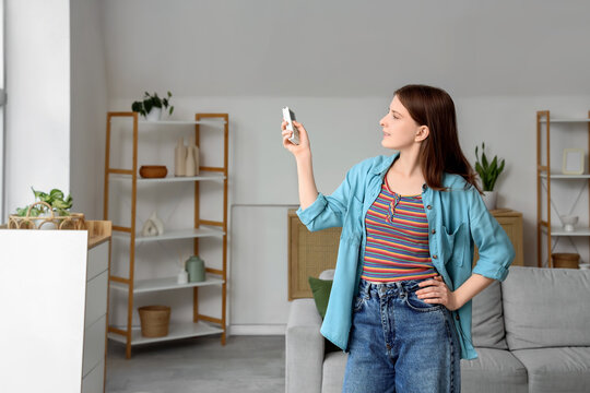 Energy efficiency and climate control, young woman using air conditioner remote at home to adjust room temperature for comfort and sustainable living