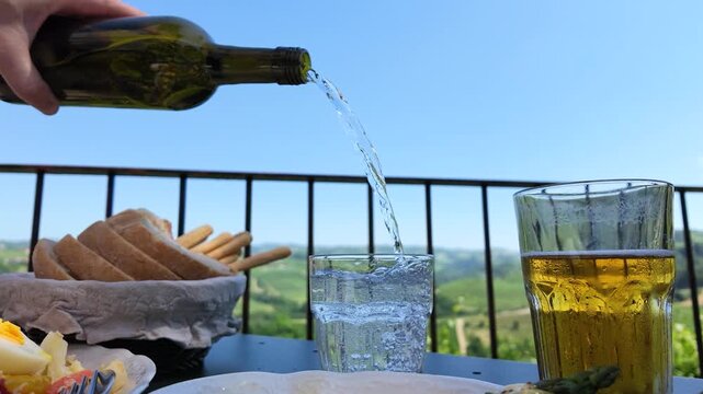 Pouring Water from Bottle into Glass at Balcony Table