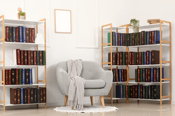 Home library and reading nook, cozy armchair with knitted throw blanket in a bright living room with bookshelves filled with vintage hardcover books © Pixel-Shot
