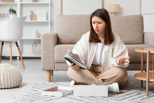 Online shopping disappointment, woman unhappy with wrong size or damaged footwear received in delivery box while sitting on living room floor at home