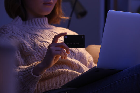 Young woman with credit card using laptop for online shopping on sofa in evening at home, closeup