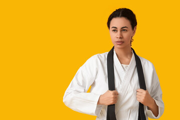 Young African-American woman with black belt practicing karate on yellow background © Pixel-Shot