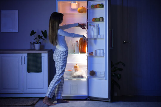 Female sleepwalker near fridge in kitchen at night