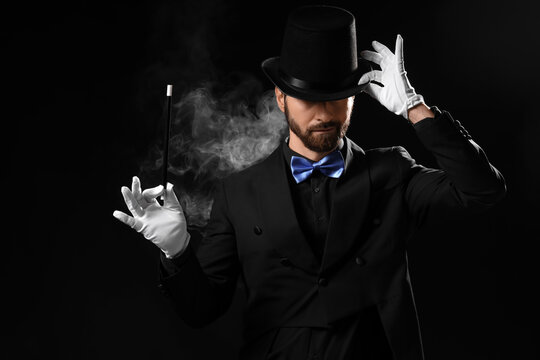 Male magician with wand and smoke on dark background