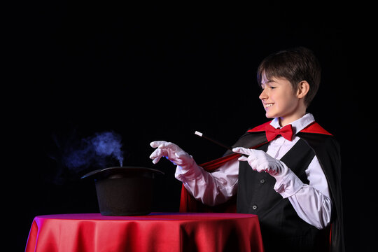 Little magician with wand and hat at table on black background