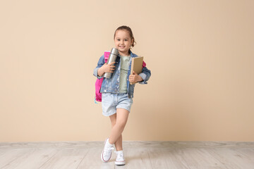 Fototapeta premium Cute little girl with adventure book and thermos near beige wall
