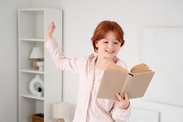 Fototapeta premium Cute teenage happy redhead girl in pajamas reading adventure book at home
