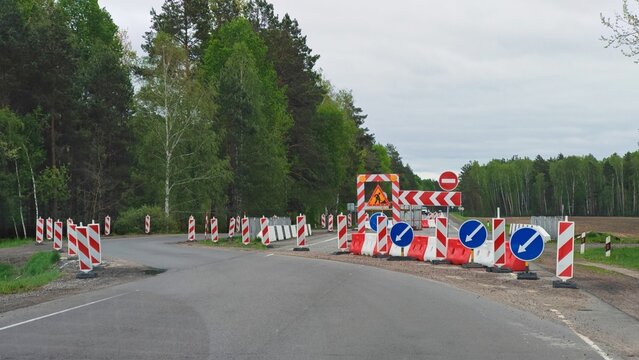 Road Construction Barriers and Signs. Road closed with red-white barriers, traffic signs and detour arrows in a forest area. Construction works.