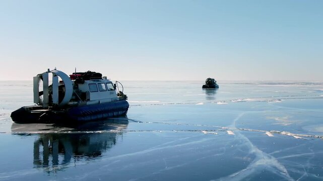 Hovercrafts moving over thin ice on frozen Baikal lake. Amphibious vehicle sliding, winter transport. Arctic transportation, extreme travel exploration in cold climate landscape. Mountains background.