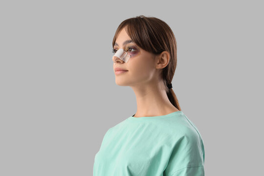 Beautiful young woman with bandaged nose on grey background. Plastic surgery concept