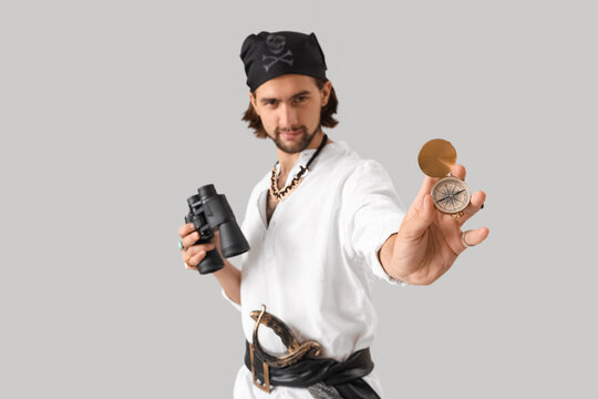 Young pirate with binoculars and compass on light background