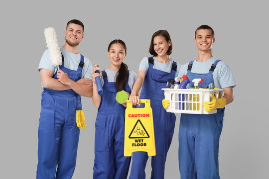 Group of young janitors with cleaning supplies on grey background