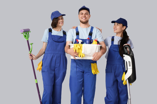 Young janitors with cleaning supplies on grey background