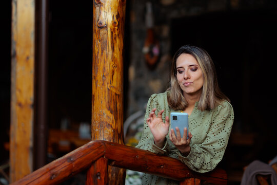 Attractive Woman Checking Dating App On Smartphone While Standing On Wooden Veranda. Blonde female makes a thoughtful face while swiping profiles on her