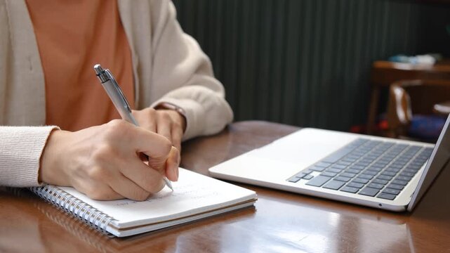 Close-up of woman writing notes in a notebook. Representing studying, work, planning, productivity and modern home office lifestyle.