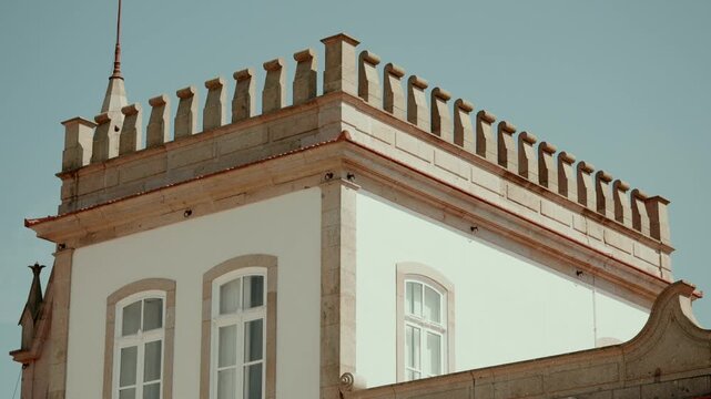 Corner of a historic manor house with a carved stone balustrade pinnacles and a lightning rod against a clear blue sky.