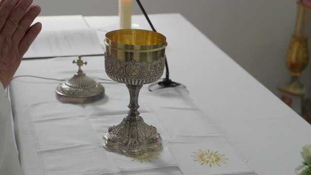 Catholic mass with priest hands over silver gilt chalice altar cloth candle and missal book
