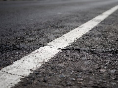 Close-up view of a painted white road marking line stretching along an asphalt surface representing travel path and transportation infrastructure