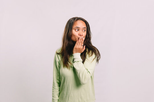 Young Southeast Asian brunette woman over isolated white background covering mouth with hand with surprised oops expression and looking away
