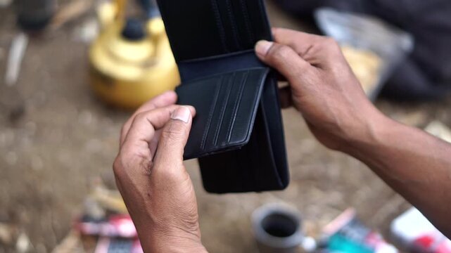 A close-up shot of someone opening an empty black leather wallet containing no cash, symbolizing a financial crisis.
