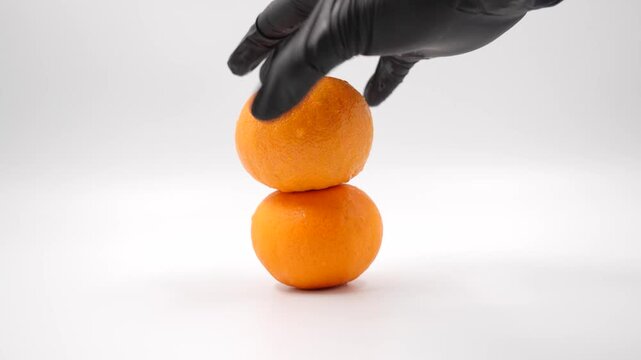 Try to stack of Fresh mandarin orange or tangerine. a black gloved hand holds an orange on a white background