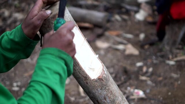 Close-up shot of a craftsman's hands carving a wooden stick using a sharp machete.