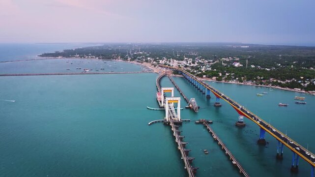 Aerial view of Pamban Bridge and the surrounding coastal landscape of Rameswaram Island, with railway tracks, turquoise sea, boats, and the shoreline of Tamil Nadu.