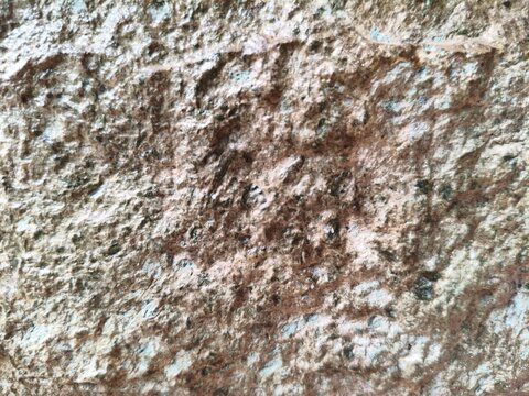 Close-up of a naturally weathered rough rock surface with detailed earthy brown, beige, gray, and subtle blue-gray mineral textures. The uneven stone pattern creates an organic and rustic abstract bac
