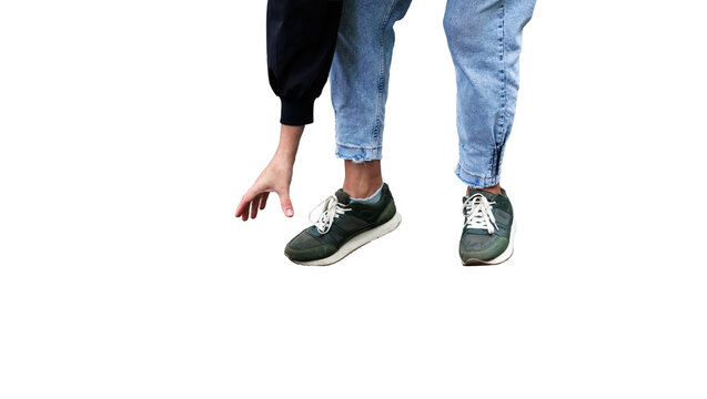 Cropped lower body of a person bending down and reaching toward the ground while wearing light blue jeans and green sneakers.