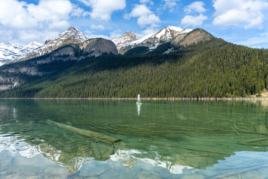 Man paddleboarding on Lake Louise with snow capped Rocky Mountains