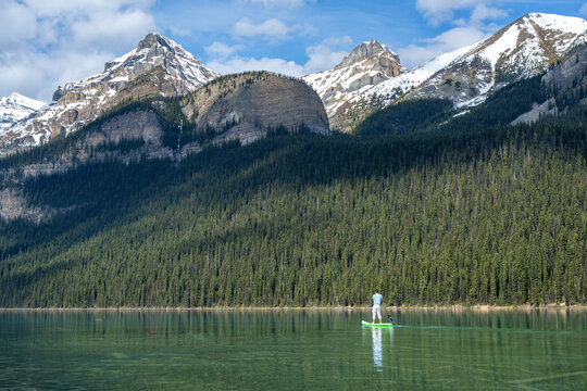 Man paddleboarding on Lake Louise with snow capped Rocky Mountains