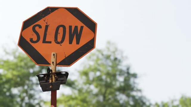 Slow down safety concept, close up of orange SLOW traffic sign with blurred trees background. 3d animation.