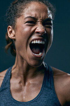 Fierce Determination A powerful close-up of a woman, glistening with sweat, her face contorted in a primal scream of effort and determination. Her eyes are squeezed shut, her jaw clenched.