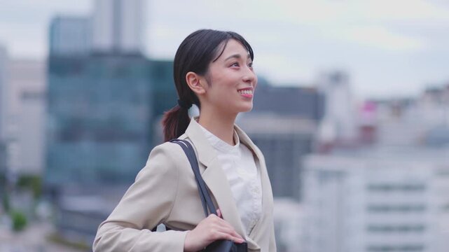 街並みを背景に前方を見つめて微笑むスーツ姿の女性 スローモーション