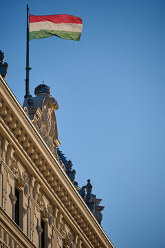 Flag of Hungary flying above the ornamental roofline of a classic building against a blue sky in Budapest