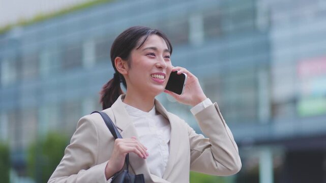 ガラス張りのビルを背に通話しながら歩く笑顔の女性 スローモーション