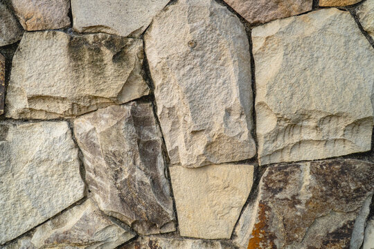 Close-up of an irregular stone wall with natural gray, beige, and brown textures and visible joints between the stones.