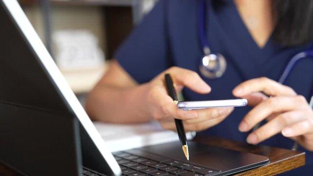 Healthcare professional uses a smartphone to review patient records, verify medical data and check digital health information on a tablet during clinical work and patient care.
