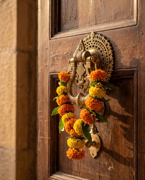 A brass door knocker adorned with a small marigold garland