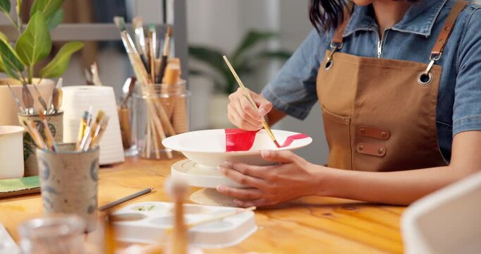 Woman, hands and painting in workshop with ceramic bowl, diy hobby or learning for skill development. Artist, person and creativity in art studio with paintbrush, craft tools and color for project.