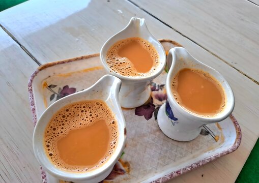 Three small ceramic pitchers filled with hot milk tea served on a floral tray