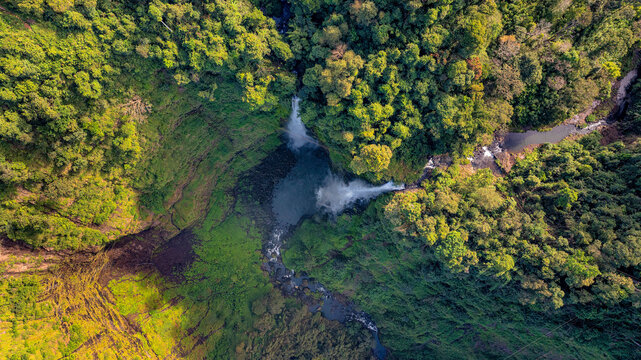 Aerial view of Tad Fane Waterfall in Laos, with a tourist enjoying tea while suspended on a zipline above the spectacular twin cascades and lush rainforest of the Bolaven Plateau.