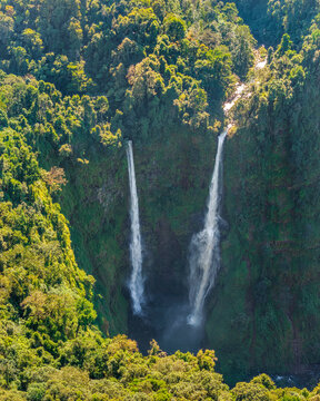 Aerial view of Tad Fane Waterfall in Laos, with a tourist enjoying tea while suspended on a zipline above the spectacular twin cascades and lush rainforest of the Bolaven Plateau.