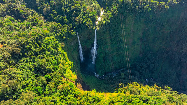 Aerial view of Tad Fane Waterfall in Laos, with a tourist enjoying tea while suspended on a zipline above the spectacular twin cascades and lush rainforest of the Bolaven Plateau.