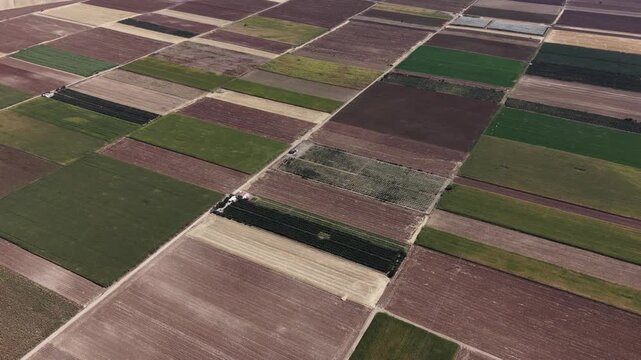Drone flying forward over multi-colored geometric farm fields in rural landscape
