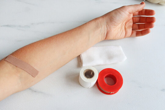 Human arm with a beige adhesive bandage on it, medical supplies on marble table, top view