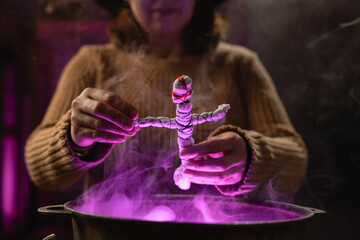 realistic witch holding voodoo doll casts spell brewing potion in cauldron. Everyday life intertwined with traditional witchcraft, magic and mystical atmosphere. © Andrii Lysenko